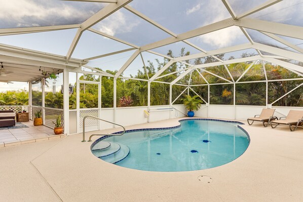 An indoor swimming pool with a glass ceiling, surrounded by lounge chairs and potted plants.