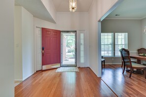 A hallway with hardwood flooring, a red door, and a dining area with a table and chairs.