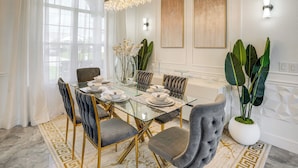 A dining room with a glass table, upholstered chairs, a chandelier, and artwork on the walls. - Upscale Treasure Coast Retreat! Port St Lucie Home (Port Saint Lucie)