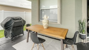 An outdoor patio with a wooden table, two chairs, a decorative vase, a grill, and a potted plant. - Upscale Treasure Coast Retreat! Port St Lucie Home (Port Saint Lucie)