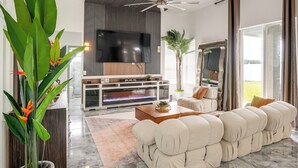 A modern living room with a flat-screen TV, a ceiling fan, a sofa, and a large plant. - Upscale Treasure Coast Retreat! Port St Lucie Home (Port Saint Lucie)