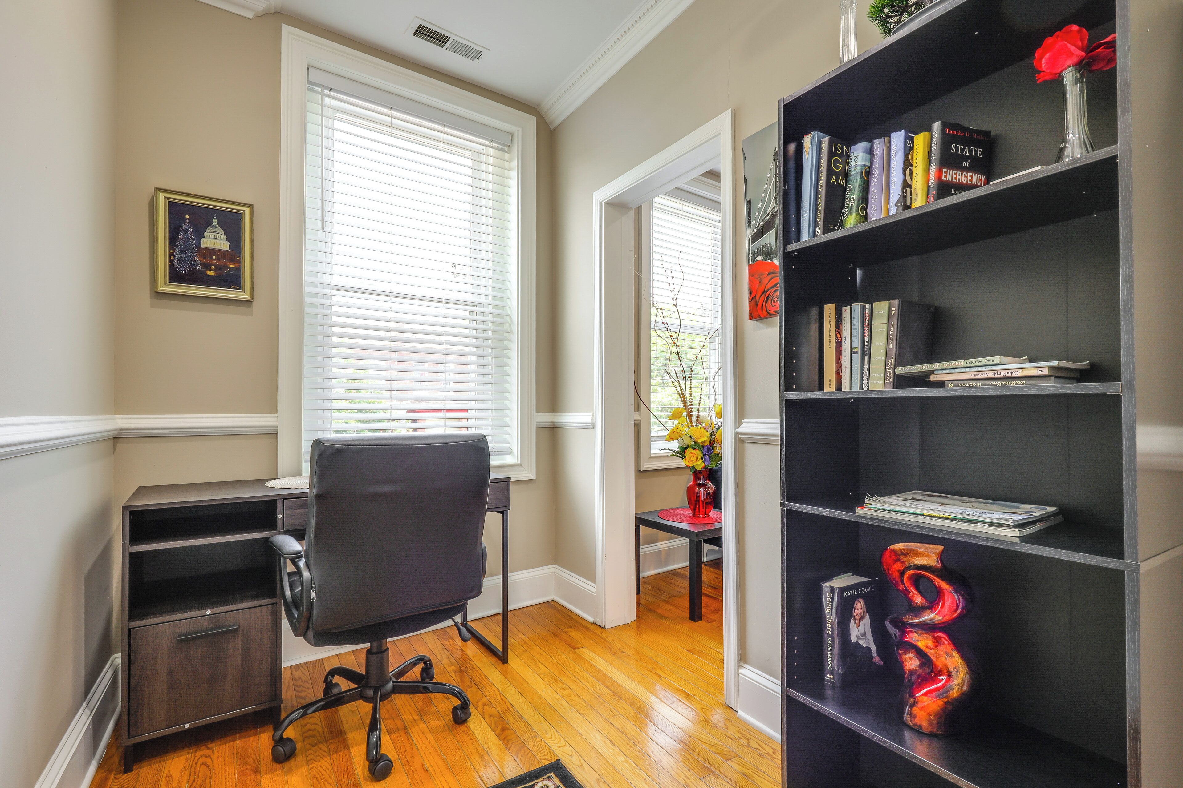 Een werkplek aan huis met een bureau, stoel, boekenkast en een ingelijst beeld aan de muur.