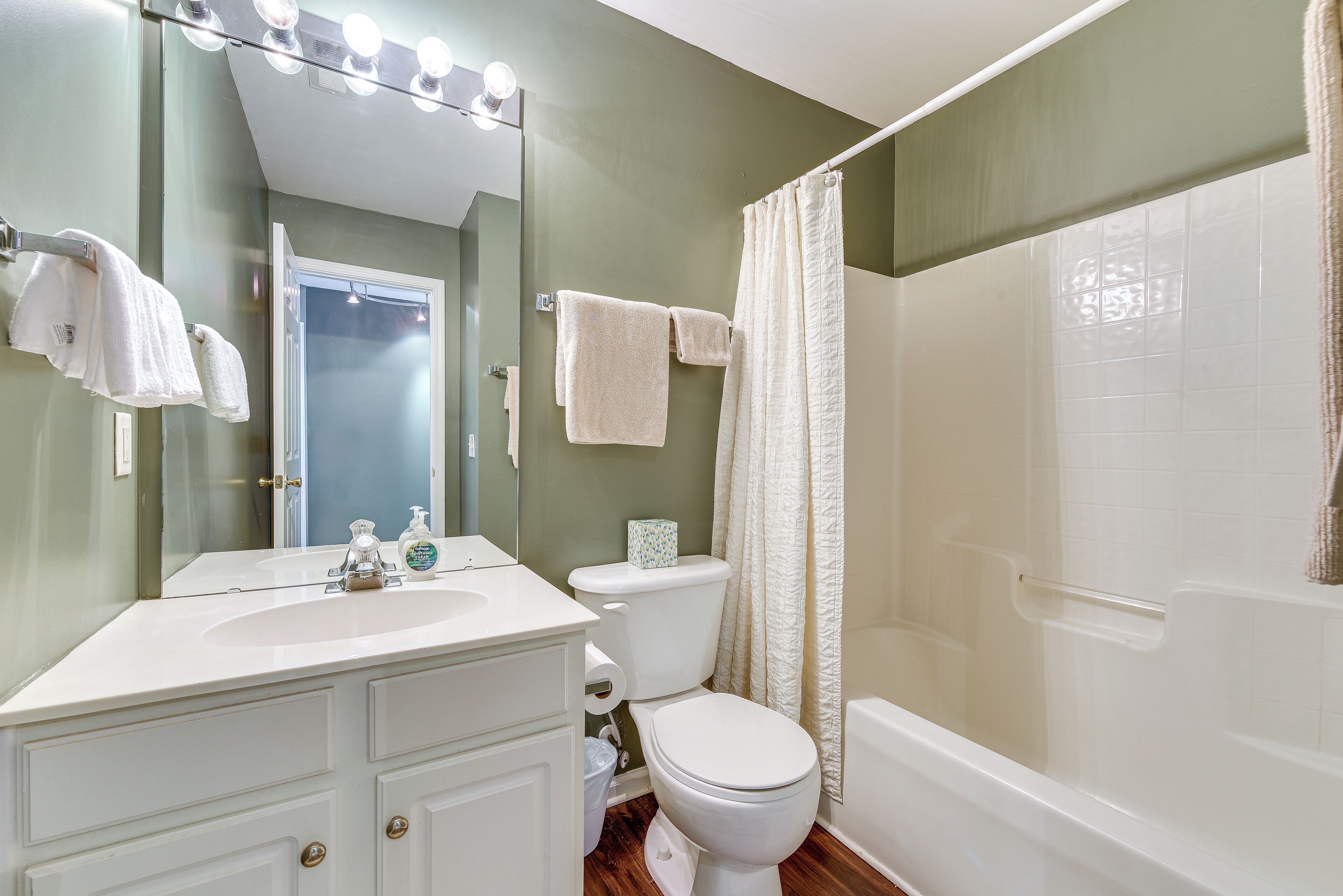 Une salle de bain avec un lavabo, des toilettes et une baignoire, tous de couleur blanche. Des serviettes sont accrochées au mur et il y a un rideau de douche.