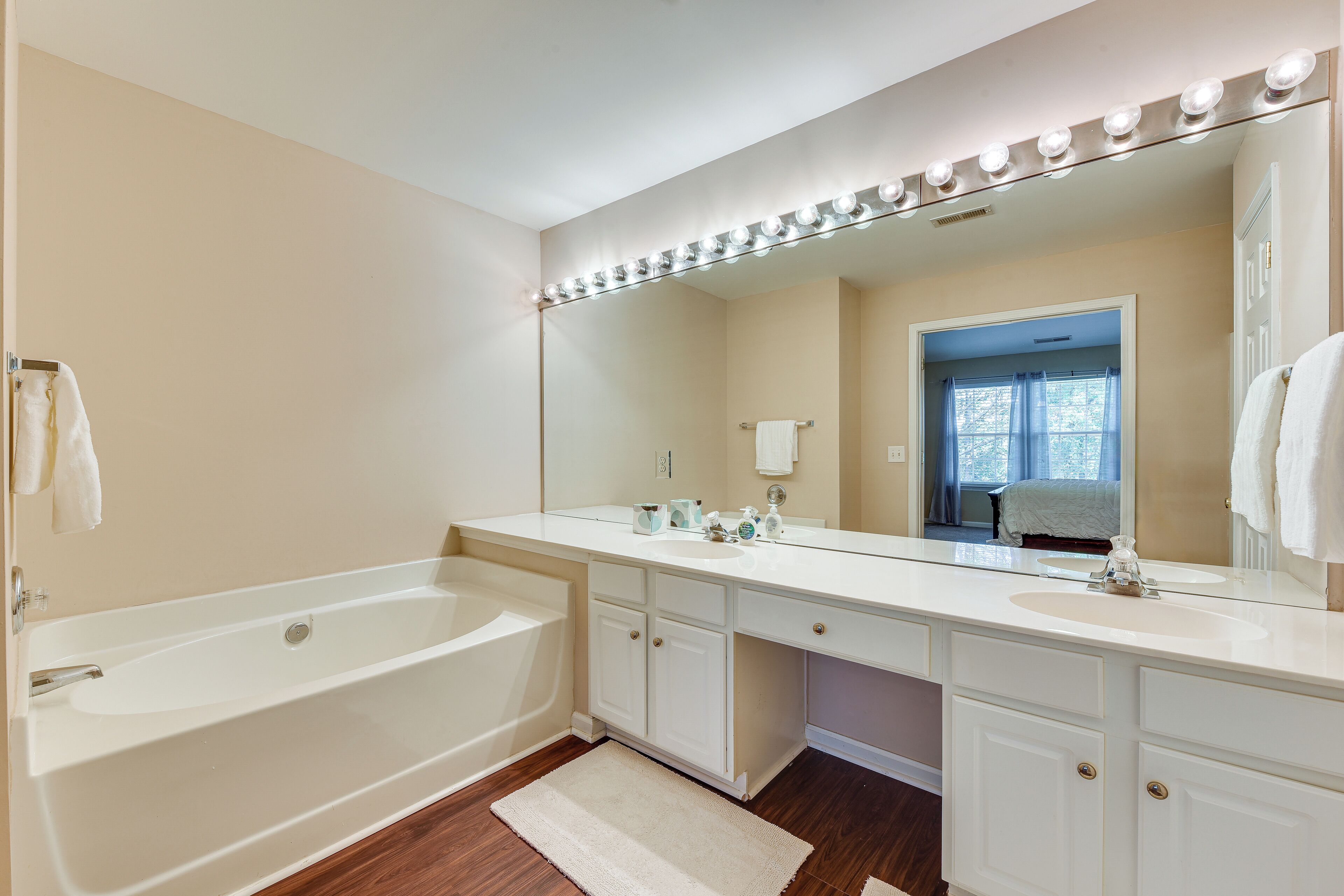 A bathroom with a bathtub, vanity with a large mirror, and a window with curtains.