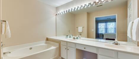 A bathroom with a bathtub, vanity with a large mirror, and a window with curtains.