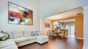 Una sala moderna con un sofá modular, un comedor con sillas y un cuadro abstracto grande en la pared.