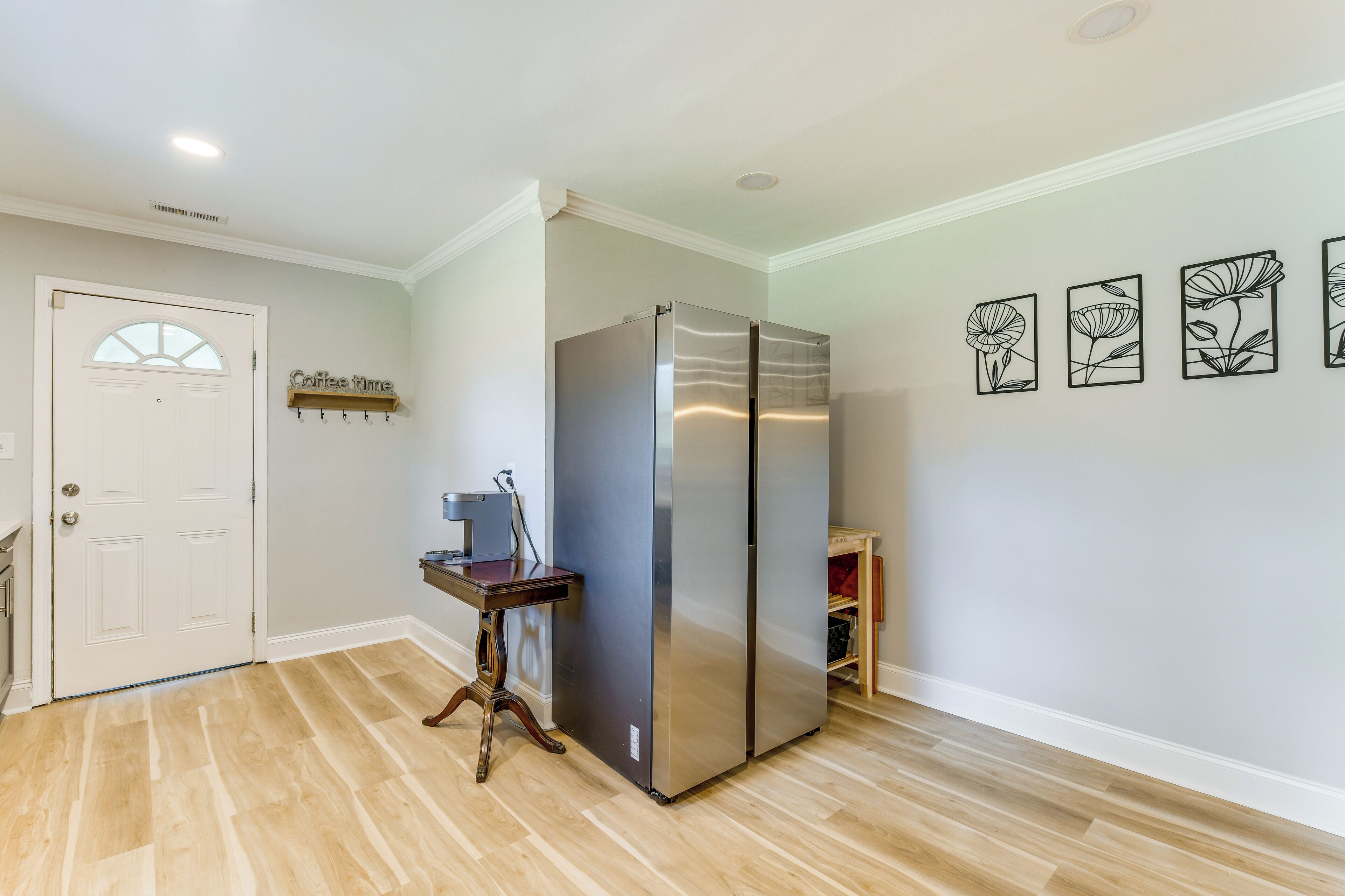 A kitchen with a stainless steel refrigerator, wooden flooring, a white door, and wall-mounted artwork.