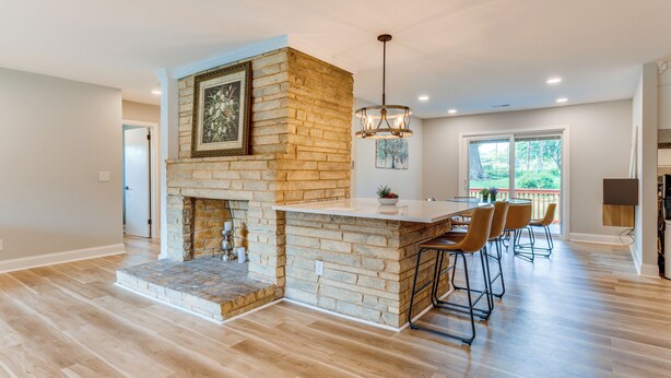 A spacious kitchen with a stone fireplace, a dining area with bar stools, and a large window providing a view of the outdoors. - Charming Charlotte Home: 2 Mi to Downtown! (Charlotte)
