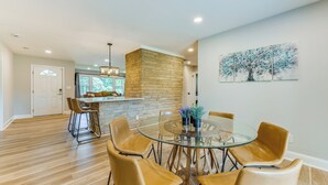 A modern dining area with a glass table surrounded by leather chairs, a stone accent wall, and a view of the kitchen. - Charming Charlotte Home: 2 Mi to Downtown! (Charlotte)