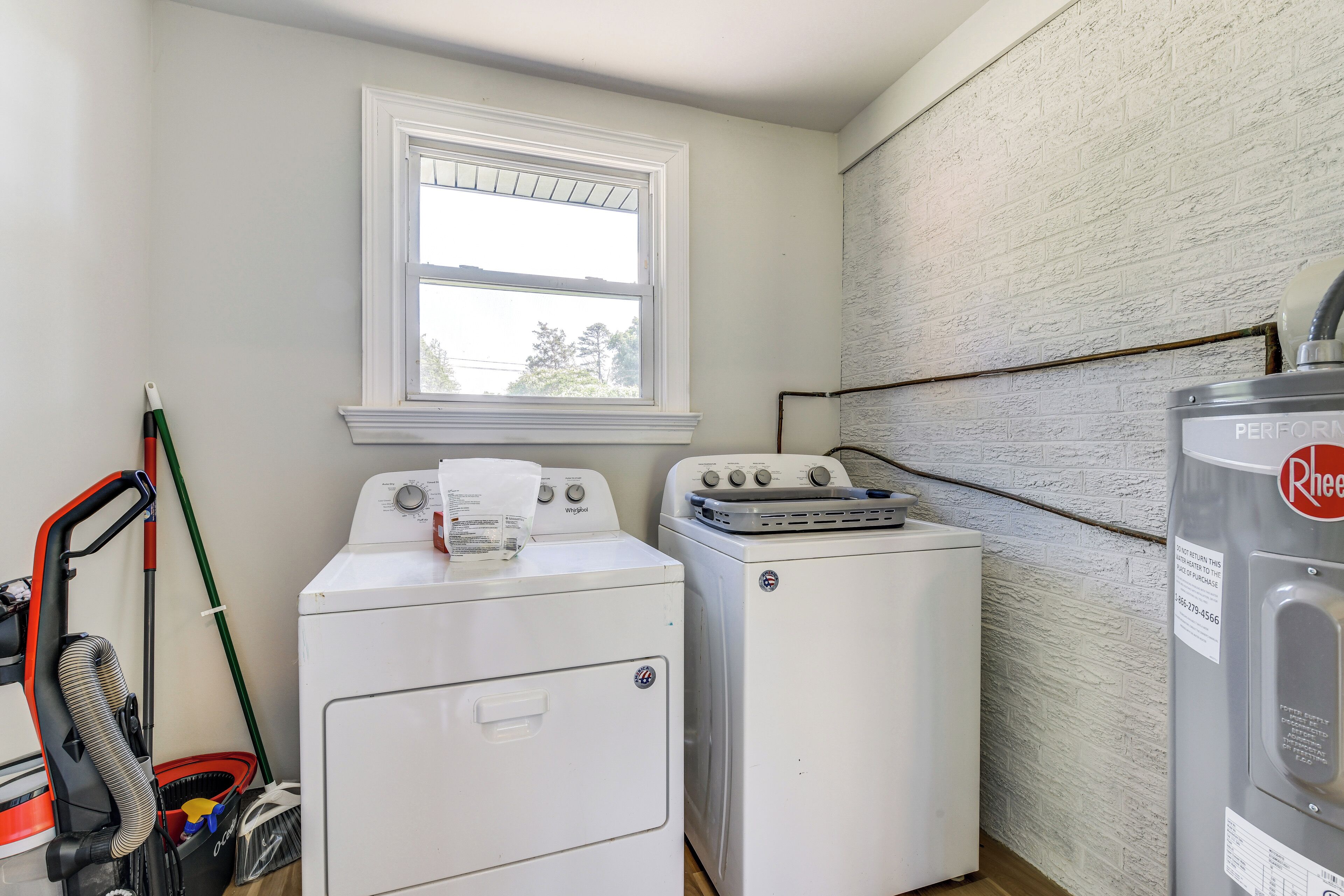 A laundry room with two white washing machines, a window, and a water heater.