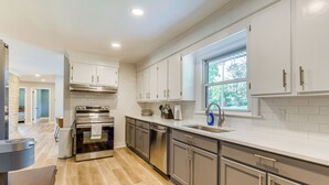A modern kitchen with stainless steel appliances, white cabinetry, and a large window providing natural light. - Charming Charlotte Home: 2 Mi to Downtown! (Charlotte)