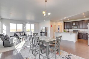 A spacious living area with a dining table, gray chairs, and a gray sofa. A kitchen with dark cabinets and modern appliances is visible in the background. - Near Rocky Mountain Arsenal: Commerce City Home (Commerce City)