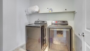 Een wasserette met twee wasmachines en drogers van roestvrij staal, een wit schapf en een deur aan de rechterkant.
