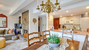 A modern living room with a wooden dining table, a chandelier, and a TV in the background. - Vail Top-floor Condo w/ Deck & Mountain Views! (Vail)
