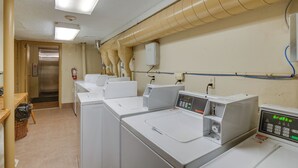 A laundry room with multiple washing machines and dryers, a fire extinguisher, and a door leading to another room. - Vail Top-floor Condo w/ Deck & Mountain Views! (Vail)