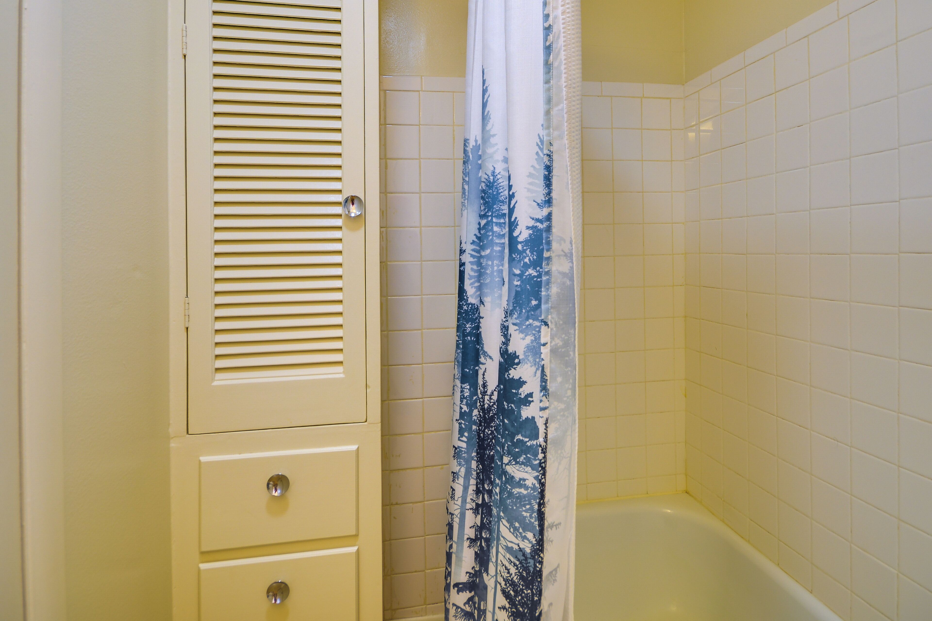 A bathroom with a white tiled wall, a white bathtub, and a door with a windowed section.