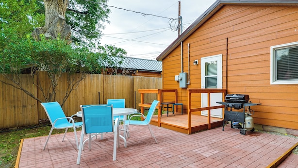 Una casa de madera con un patio que cuenta con una mesa, sillas, una parrilla y una terraza de madera.