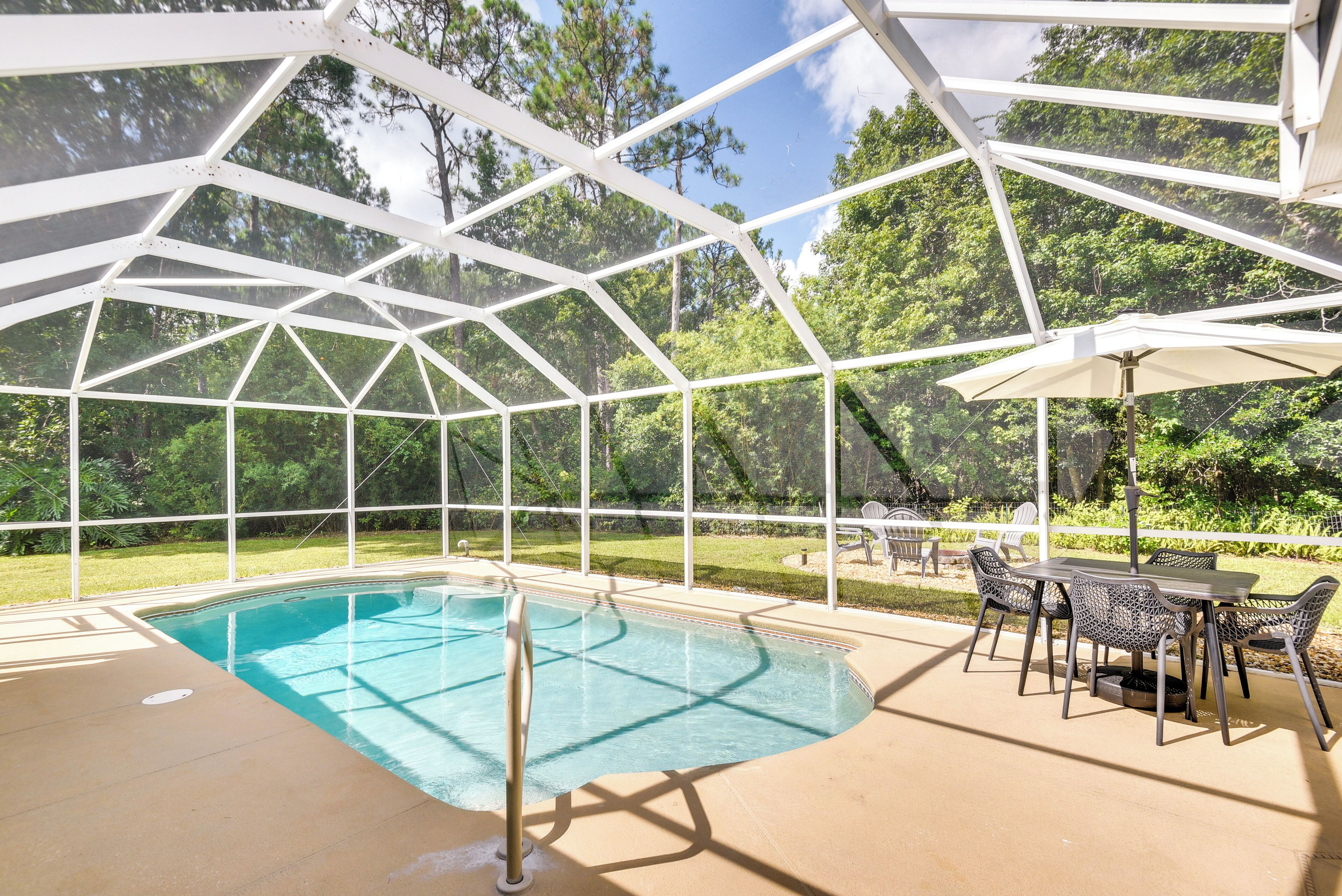 A covered outdoor pool with a table and chairs, surrounded by a white metal frame and glass panels.