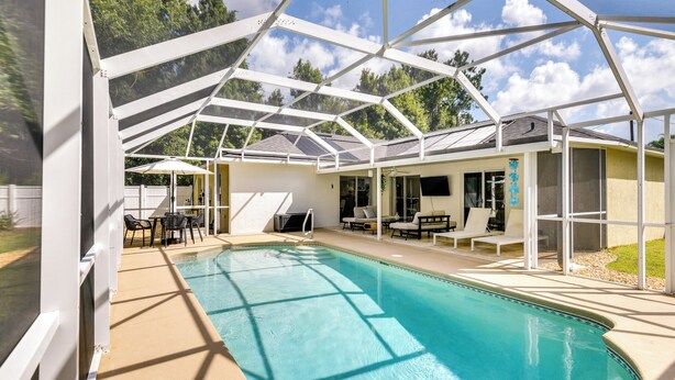 Une piscine couverte avec un toit en verre, entourée de chaises longues et d’un espace patio.