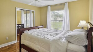 A bedroom with a bed, a ceiling fan, a window with curtains, and a lamp. - Palm Coast Escape: Screened Lanai, Saltwater Pool! (Palm Coast)
