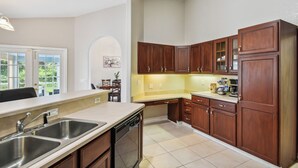 A kitchen with wooden cabinets, a dishwasher, and a window overlooking a garden. - Palm Coast Escape: Screened Lanai, Saltwater Pool! (Palm Coast)