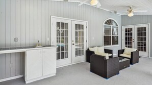 A covered outdoor area with a white wooden wall, a built-in bar, two doors with windows, and a ceiling fan. - Palm Coast Escape: Screened Lanai, Saltwater Pool! (Palm Coast)