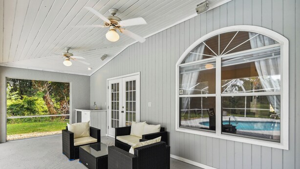 A covered patio with wicker furniture, a ceiling fan, and a view of a swimming pool. - Palm Coast Escape: Screened Lanai, Saltwater Pool! (Palm Coast)