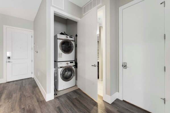 A laundry room with two stacked front-loading washers and dryers, a white door, and a wooden floor. - 5 Mi to Red Rocks! Updated Home Near Hiking Trails (Golden)