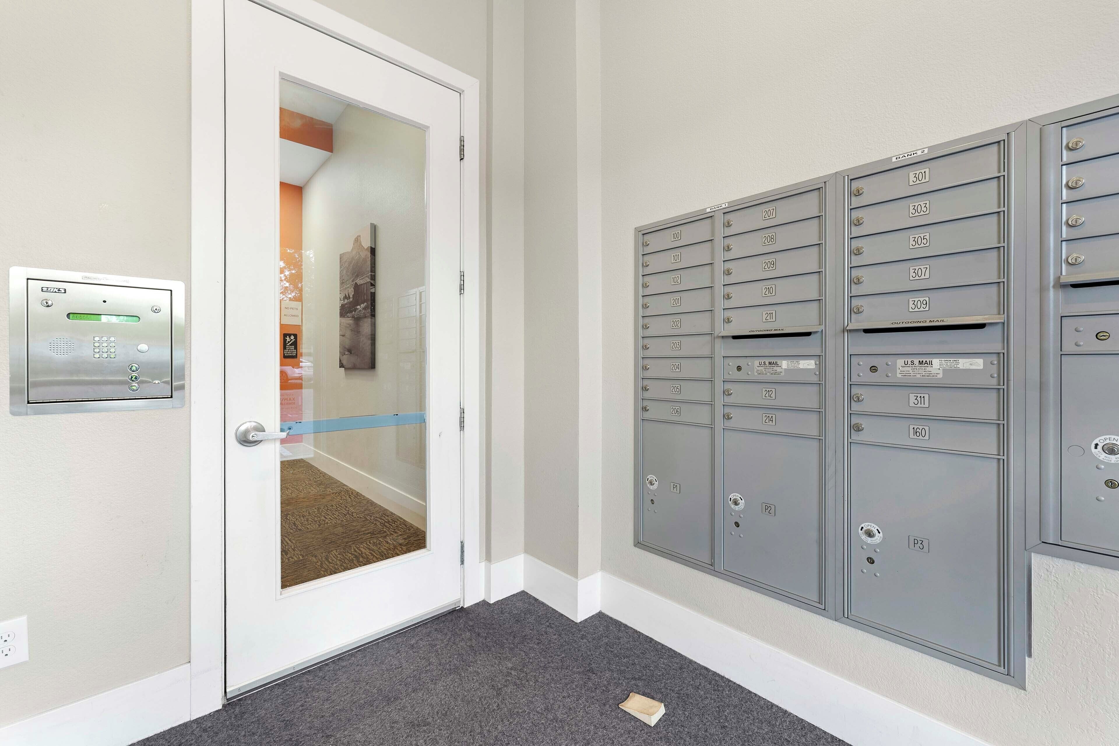 Un pasillo con una puerta que da a una habitación, un buzón y una fila de casilleros de correo.