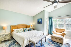A bedroom with a bed, bench, chair, nightstand, lamp, and artwork on the wall.