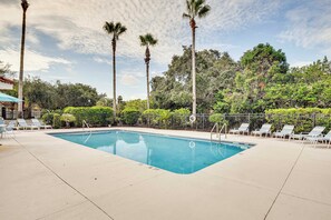 A rectangular pool with a clear blue water surface, surrounded by white lounge chairs and palm trees.