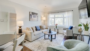 Un salon comprenant un canapé, une table basse et des fauteuils, une table à manger, un ventilateur de plafond et une fenêtre avec des rideaux.