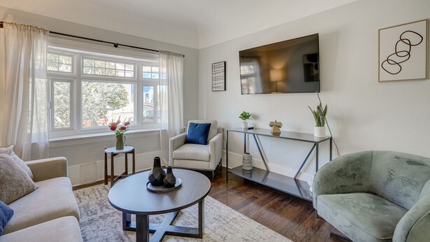 Un salon moderne avec un canapé, un fauteuil, une table basse et un téléviseur fixé au mur.