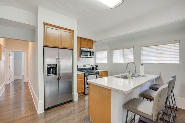 A modern kitchen with stainless steel appliances, wooden cabinets, and a bar area with stools.