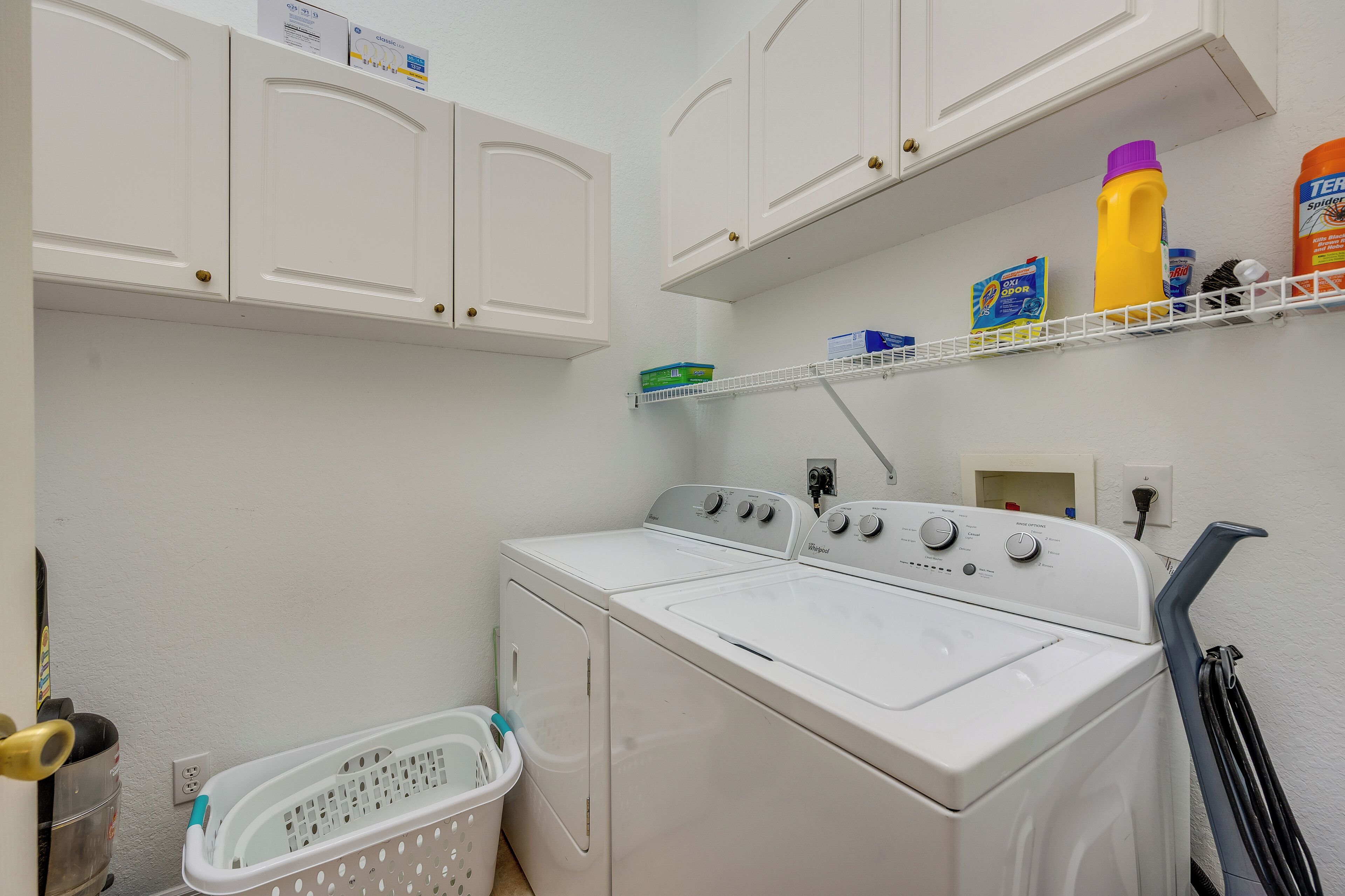 A laundry area with a front-loading washer and dryer, a laundry basket, and shelves with cleaning supplies.