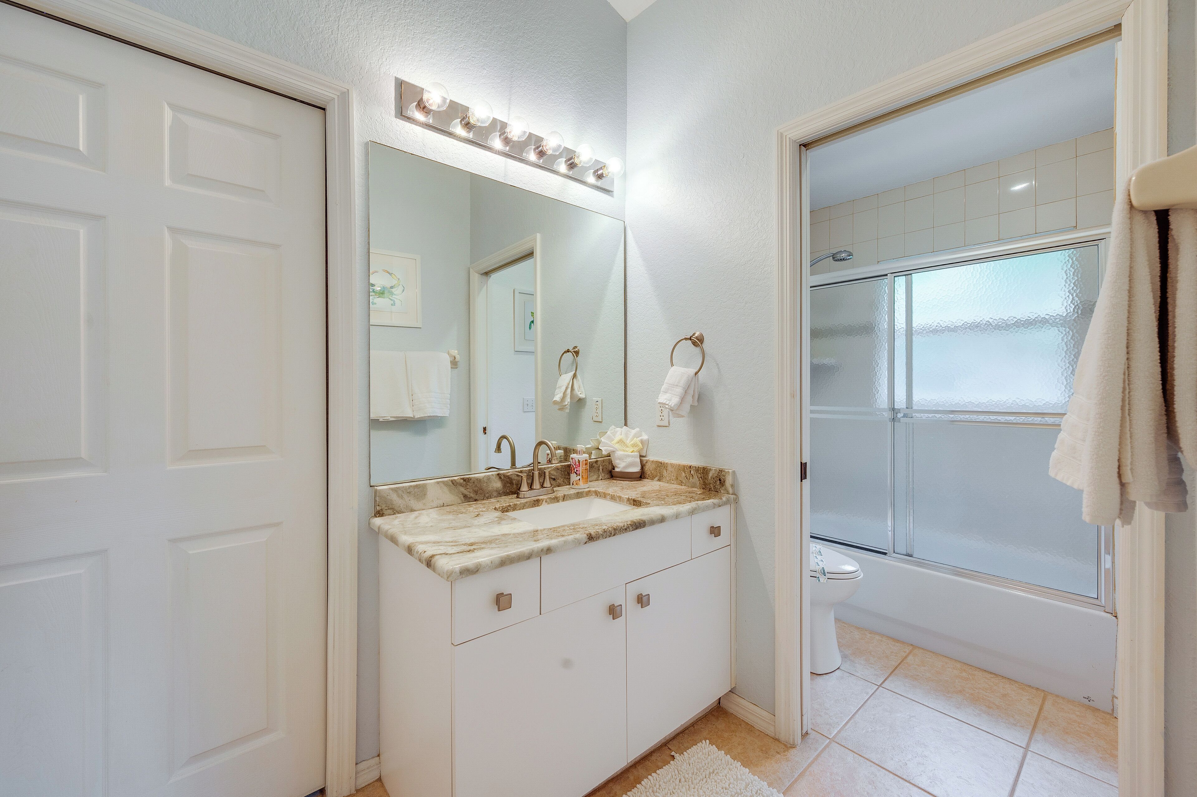 A bathroom with a white vanity, a large mirror with lights, a shower, and a toilet.