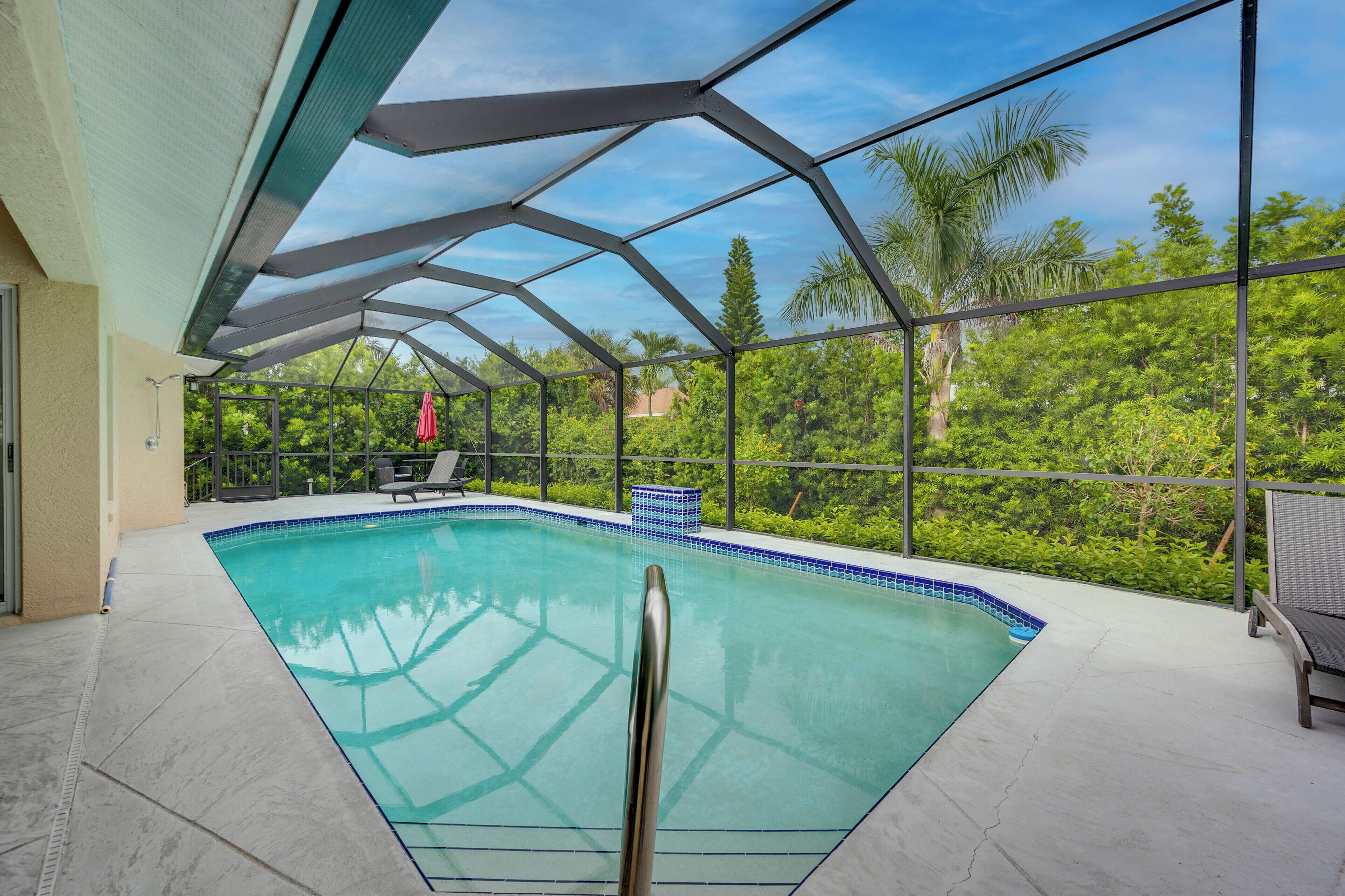 A swimming pool with a glass enclosure, surrounded by greenery and a clear sky.