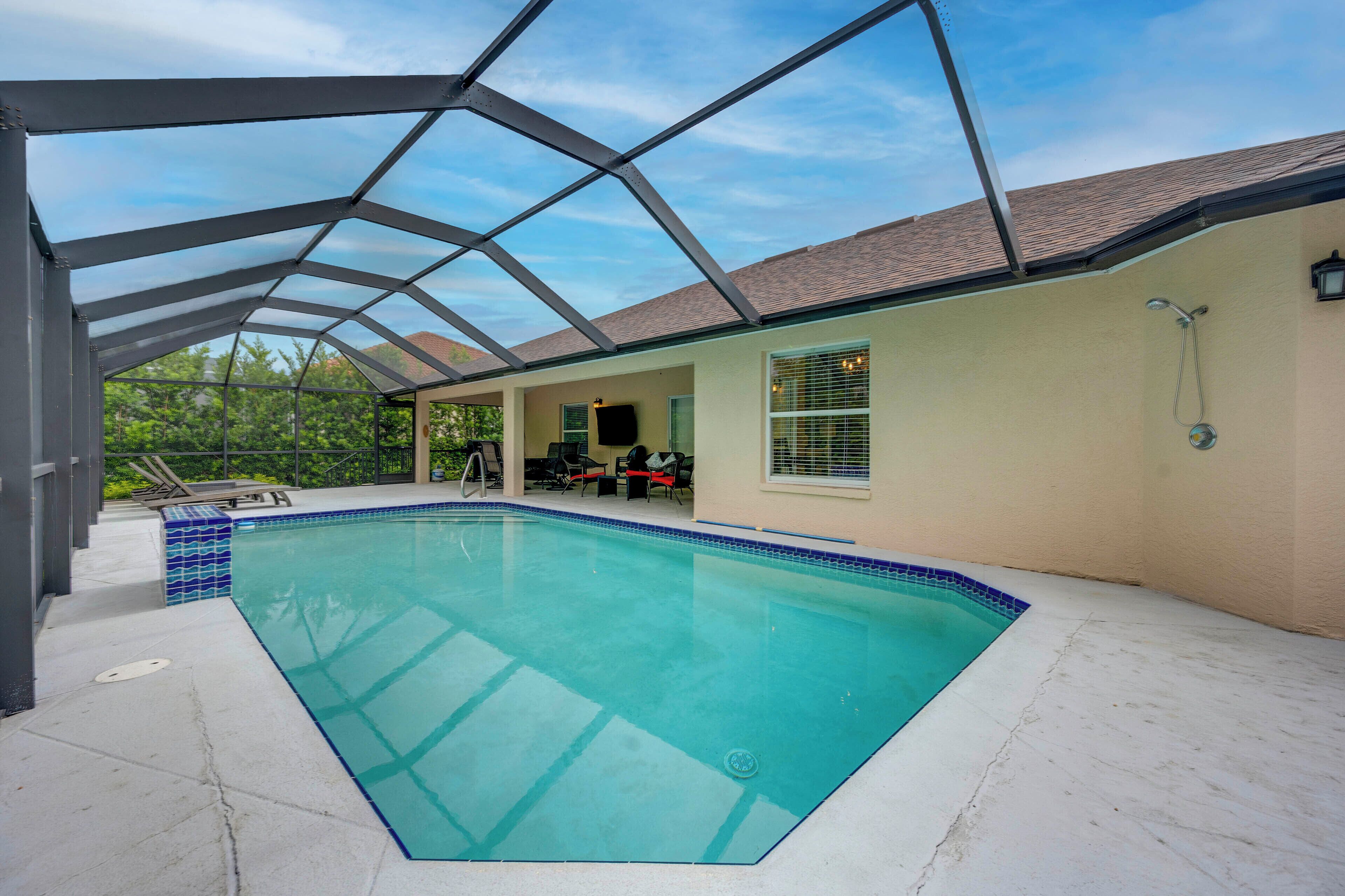 Een overdekt zwembad met glazen dak, een loungegedeelte met stoelen en uitzicht op de omgeving.