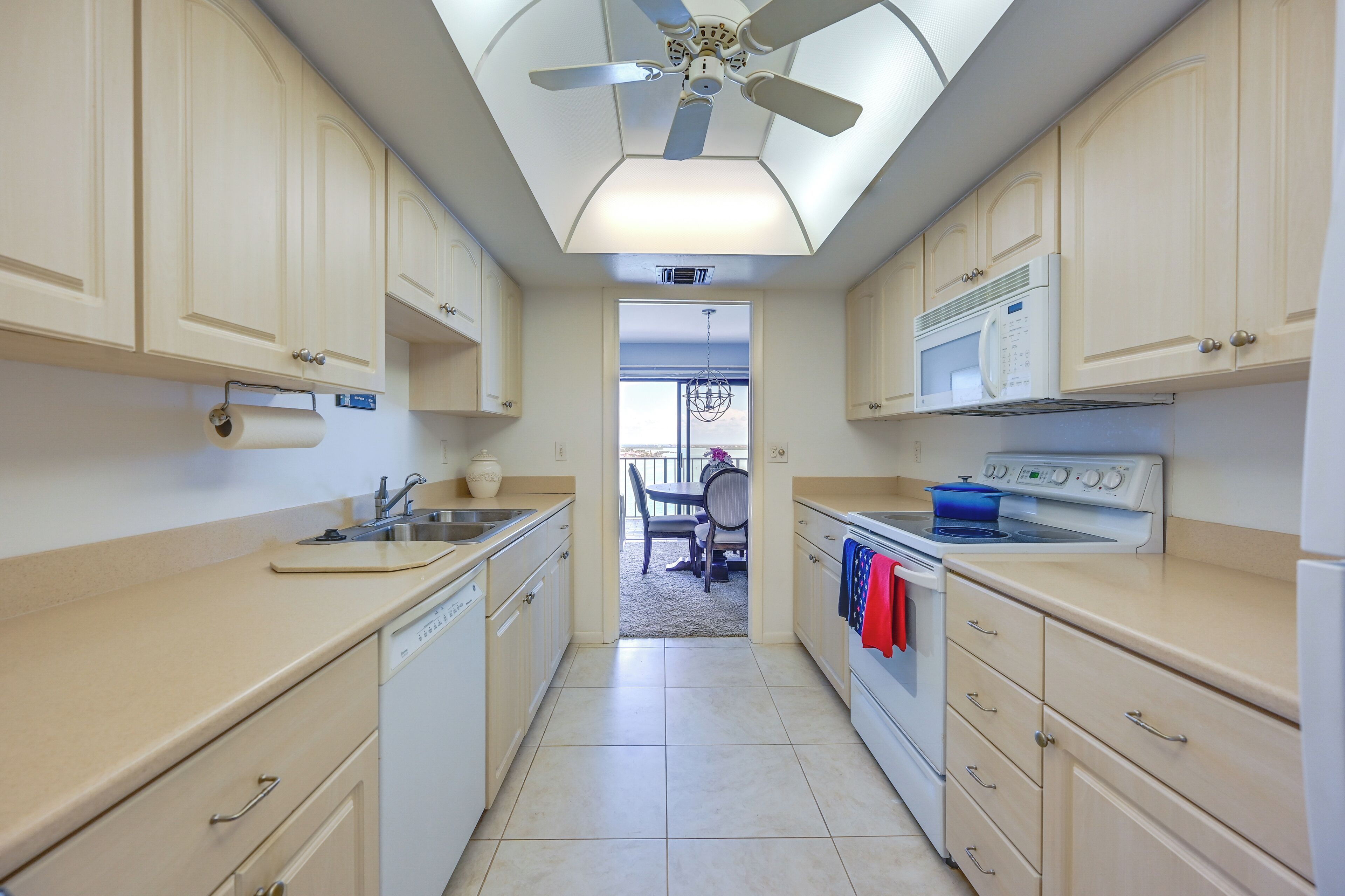 A modern kitchen with beige cabinetry, a ceiling fan, a microwave, and a stove.