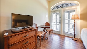 A hotel room with a flat-screen TV, wooden furniture, a dining table, and a lamp. - Close to Parks & Beaches! Naples Studio w/ Pool (Naples)