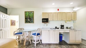 Una cocina compacta con zona de comedor, que incluye una mesa de vidrio, sillas de mimbre y armarios de madera clara.