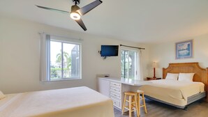 Une chambre avec deux lits, un bureau, une chaise, un ventilateur de plafond et un téléviseur.