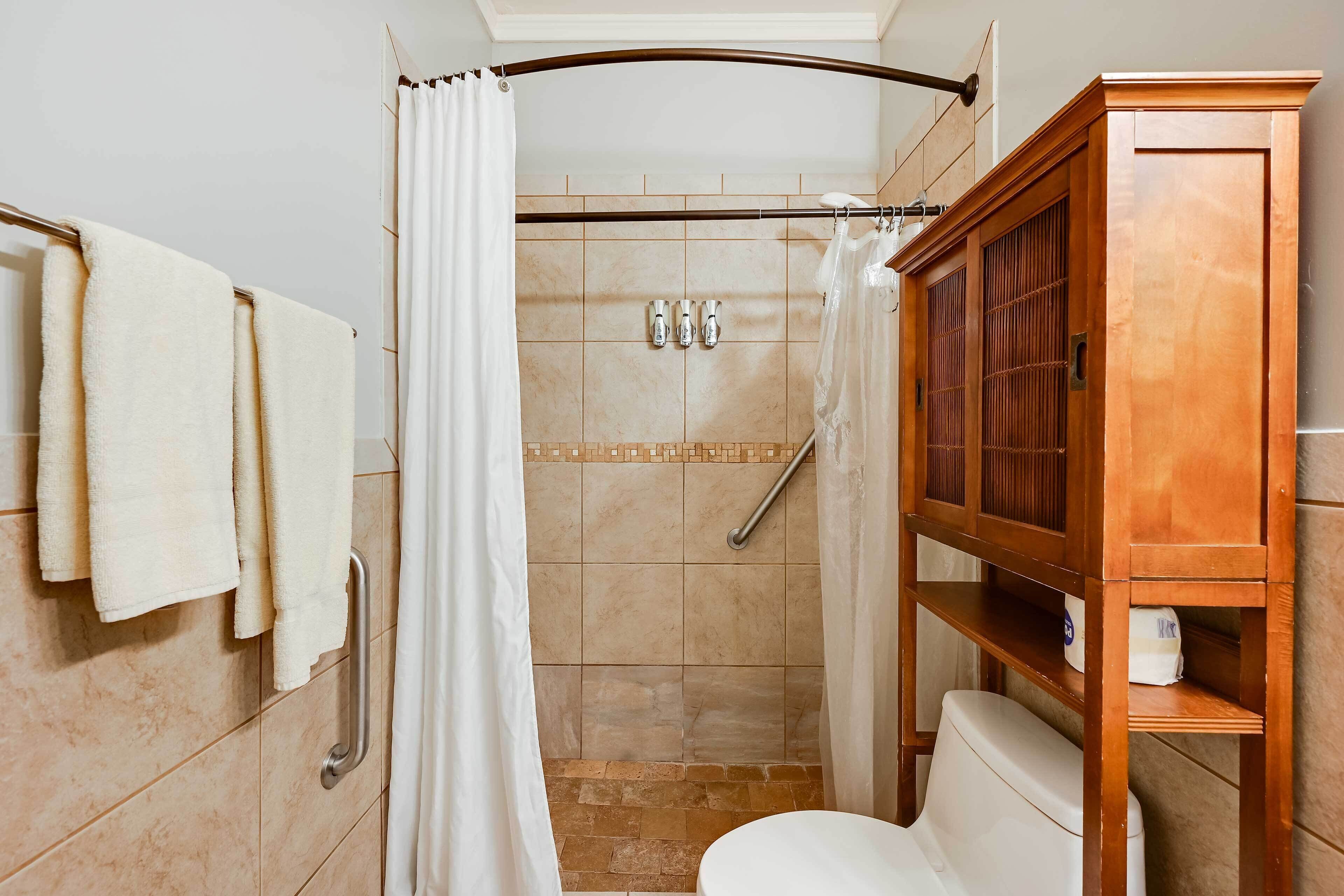 A bathroom with a shower, toilet, and a wooden cabinet.