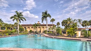 A swimming pool with a brick border, palm trees, and a building with a tiled roof in the background. - Naples Vacation Rental w/ Grill, Resort Pool! (Naples)