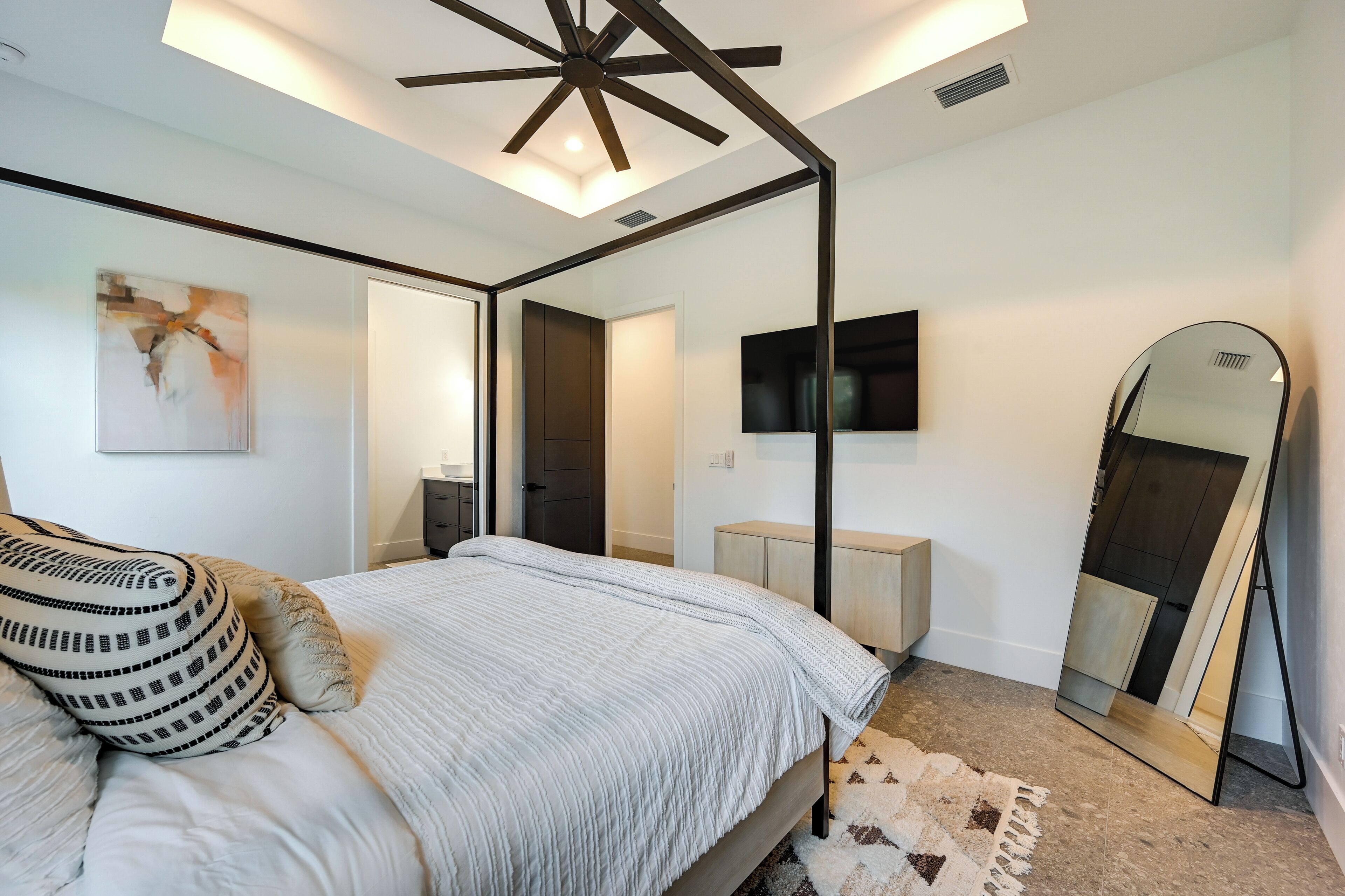Une chambre moderne avec un lit à baldaquin, un grand miroir, un téléviseur à écran plat et un ventilateur de plafond.