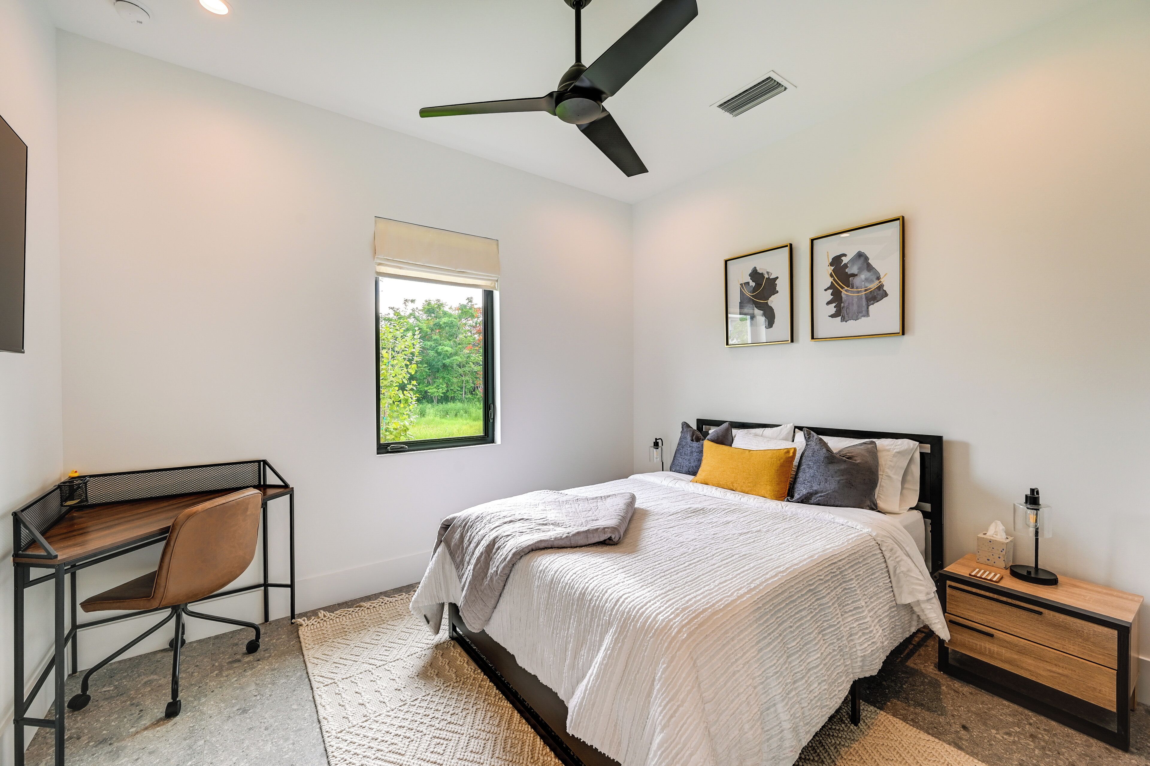 A bedroom with a bed, a desk, a chair, a nightstand, and a ceiling fan.