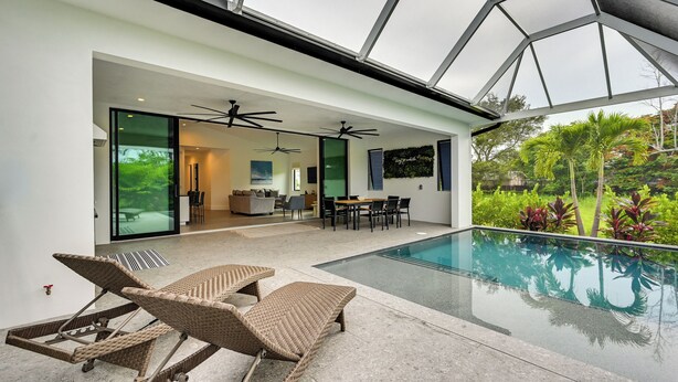 A modern indoor pool area with lounge chairs, ceiling fans, and a view of the outdoors. - Contemporary Naples Home w/ Outdoor Kitchen & Pool (Naples)