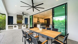 A modern kitchen with a large island, built-in appliances, and a dining area with a large table and chairs. - Contemporary Naples Home w/ Outdoor Kitchen & Pool (Naples)
