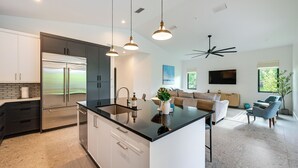 A modern kitchen with a large island, stainless steel appliances, and pendant lighting. - Contemporary Naples Home w/ Outdoor Kitchen & Pool (Naples)