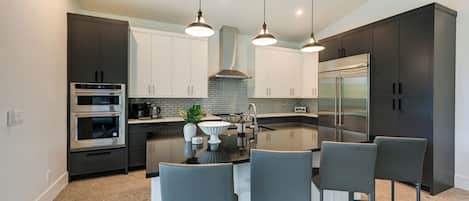 A modern kitchen with dark cabinets, stainless steel appliances, and a central island with bar stools.